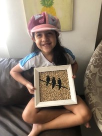 Filha mais nova mostra o quadro das Andorinhas, atividade escolar feita com grãos de feijão